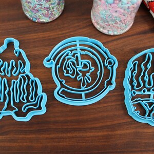 Puede incluir: Tres cortadores de galletas de pl&aacute;stico azul, uno con forma de mano, otro con forma de c&iacute;rculo con un dise&ntilde;o en el interior y otro con forma de monta&ntilde;a.