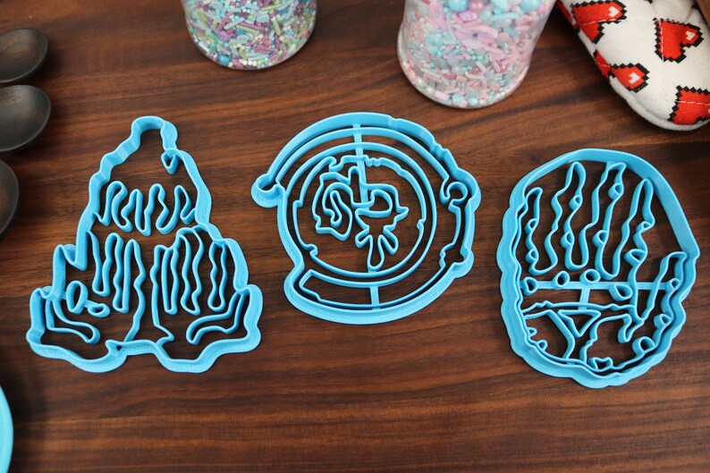 Puede incluir: Tres cortadores de galletas de pl&aacute;stico azul, uno con forma de mano, otro con forma de c&iacute;rculo con un dise&ntilde;o en el interior y otro con forma de monta&ntilde;a.