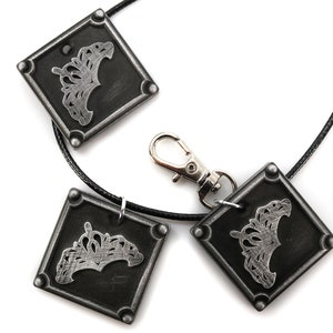 May include: A black leather necklace with three silver square pendants. Each pendant features a silver crown design.