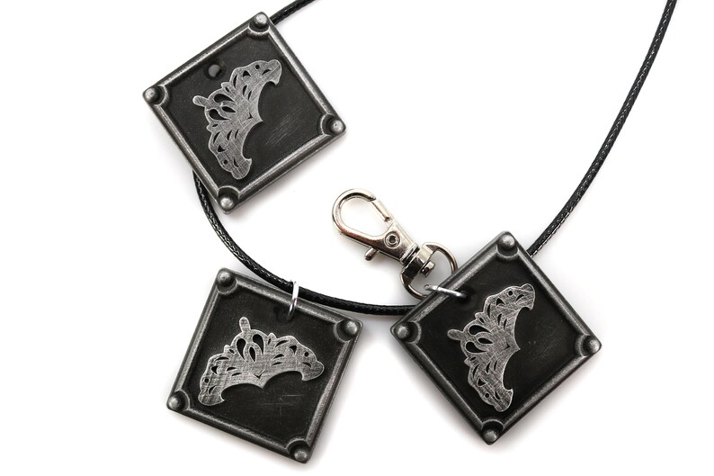 May include: A black leather necklace with three silver square pendants. Each pendant features a silver crown design.
