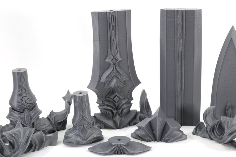May include: A set of eight gray 3D printed pieces that can be assembled into a sword. The pieces are detailed with intricate designs and have a smooth, matte finish.