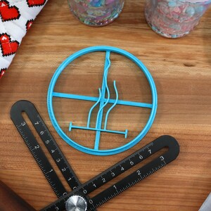 May include: A blue plastic cookie cutter shaped like a stylised flame with a cross-shaped design inside. The cutter is on a wooden surface.