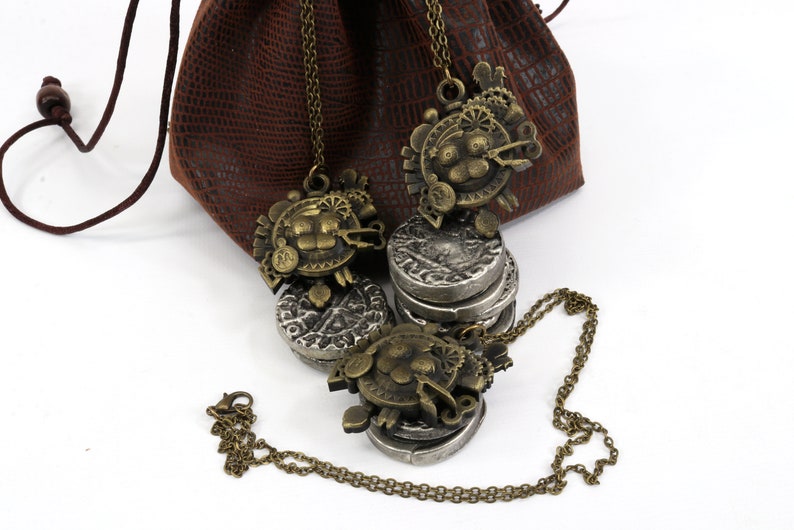 May include: A set of three silver and bronze necklaces with intricate designs. The necklaces are displayed on a brown leather pouch with a drawstring closure.