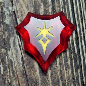 May include: A red and silver shield-shaped charm with a yellow starburst design in the centre.