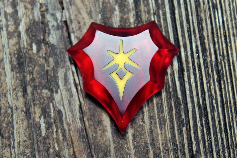 May include: A red and silver shield-shaped charm with a yellow starburst design in the centre.