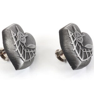 K&ouml;nnte beinhalten: Zwei silberne herzf&ouml;rmige Anstecknadeln mit einem detaillierten Design aus einem Kreuz und Bl&auml;ttern. Die Anstecknadeln haben eine silberne Metallnadelr&uuml;ckseite.