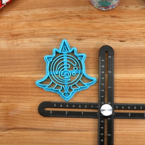 May include: A blue plastic cookie cutter shaped like a stylized sun with a swirling design inside. The cutter is about 2 inches in diameter and is sitting on a wooden surface.