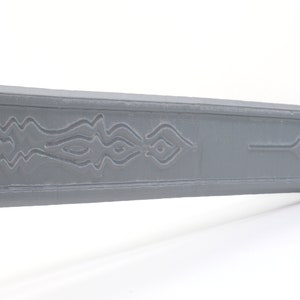 May include: A gray plastic sword with a decorative design on the blade. The design features a series of wavy lines and a symbol at the end of the blade.