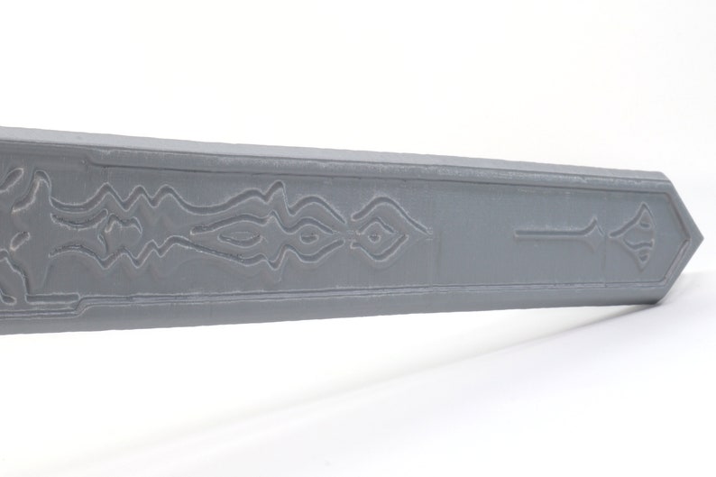May include: A gray plastic sword with a decorative design on the blade. The design features a series of wavy lines and a symbol at the end of the blade.