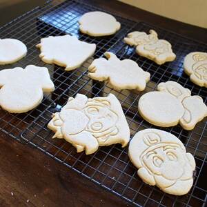 May include: A cooling rack with nine plain sugar cookies, some with cartoon characters, others with simple shapes.