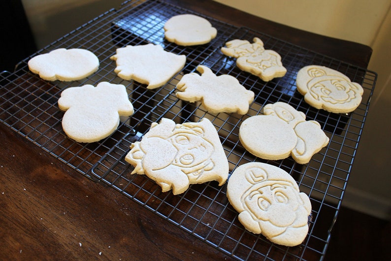 May include: A cooling rack with nine plain sugar cookies, some with cartoon characters, others with simple shapes.