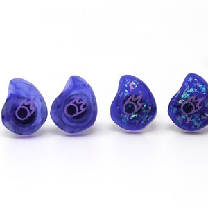 May include: Four pairs of custom-molded purple earplugs with a purple flame logo. Two pairs have a glittery finish.