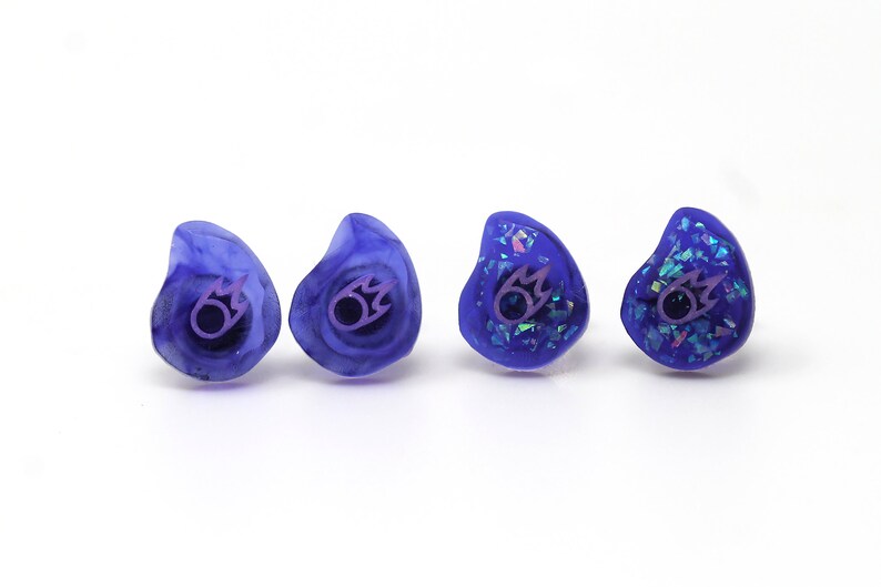 May include: Four pairs of custom-molded purple earplugs with a purple flame logo. Two pairs have a glittery finish.