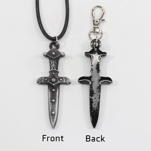 May include: A silver dagger pendant with intricate details on the hilt, shown on a black cord necklace and as a keychain. The dagger has a distressed, aged look.
