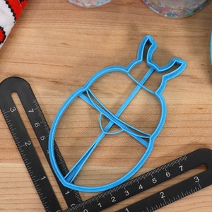 May include: A blue plastic cookie cutter shaped like a beetle with a raised design. The cutter is approximately 5 cm in diameter.