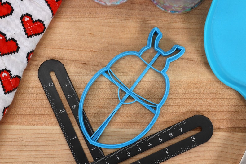 May include: A blue plastic cookie cutter shaped like a beetle with a raised design. The cutter is approximately 5 cm in diameter.