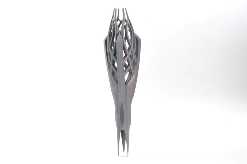 May include: A 3D printed, gray, abstract sculpture with a geometric, lattice-like design. The sculpture is tall and narrow, with a pointed top and a base that is slightly wider than the top.