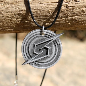 May include: A silver-colored metal necklace with a pendant featuring the iconic Super Smash Bros. logo. The pendant is circular with a stylized 'S' and a lightning bolt design.