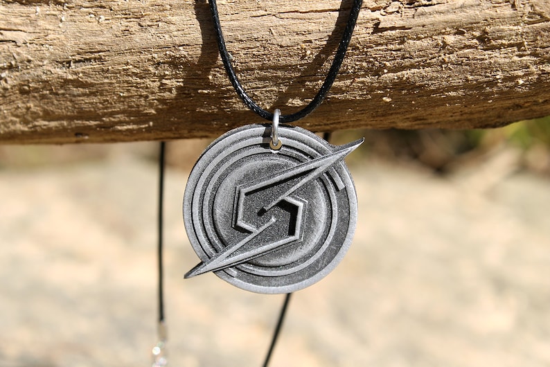 May include: A silver-colored metal necklace with a pendant featuring the iconic Super Smash Bros. logo. The pendant is circular with a stylized 'S' and a lightning bolt design.