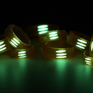 May include: A group of glow-in-the-dark rings with white stripes. The rings are stacked on top of each other and are glowing green.