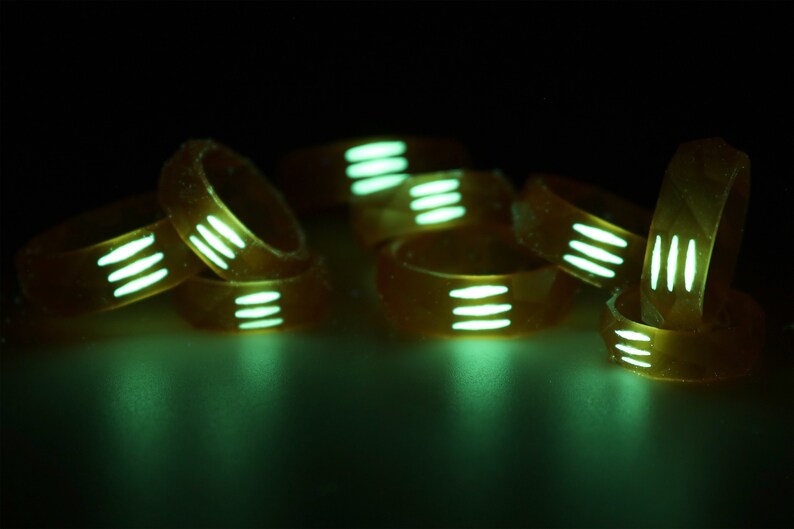 May include: A group of glow-in-the-dark rings with white stripes. The rings are stacked on top of each other and are glowing green.