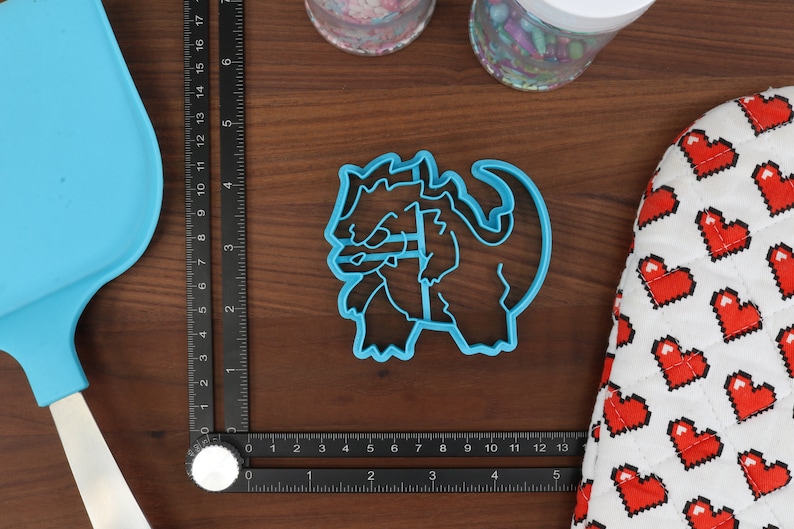 May include: A blue plastic cookie cutter shaped like a cartoon dragon. The dragon is curled up with its head resting on its front paws.