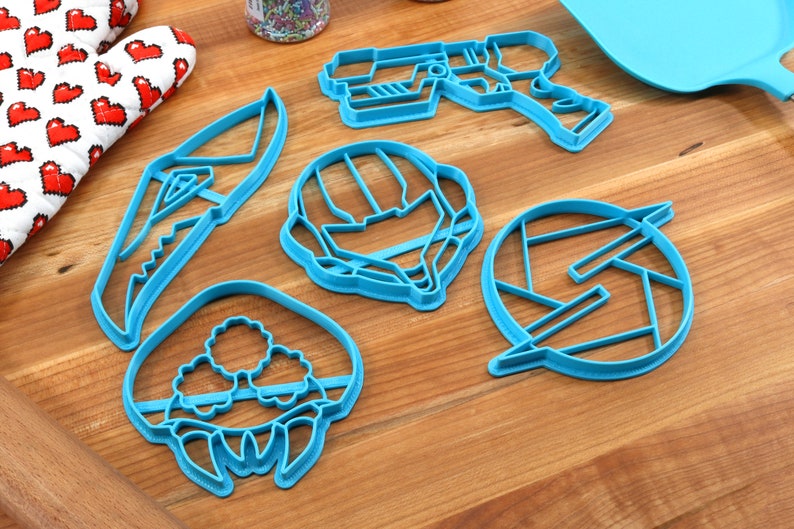 May include: Five blue plastic cookie cutters shaped like a space helmet, a gun, a creature, a knife, and a symbol.