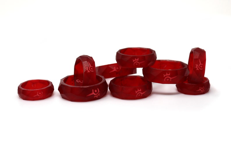 May include: A group of nine red rings with a white design. The rings are stacked and scattered on a white surface.