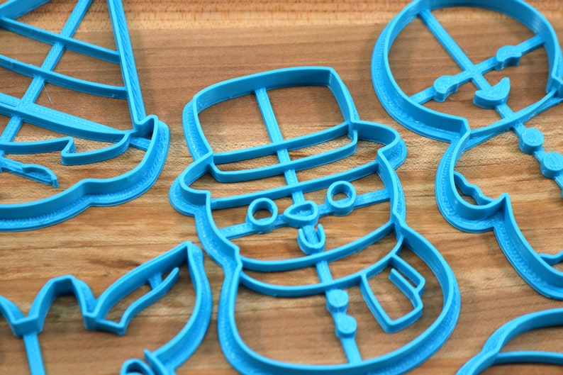 Op de afbeelding: Een set van vier blauwe plastic koekjesvormen in de vorm van een sneeuwpop, een kerstboom, een snoepstok en een rendier. De vormen liggen op een houten oppervlak.