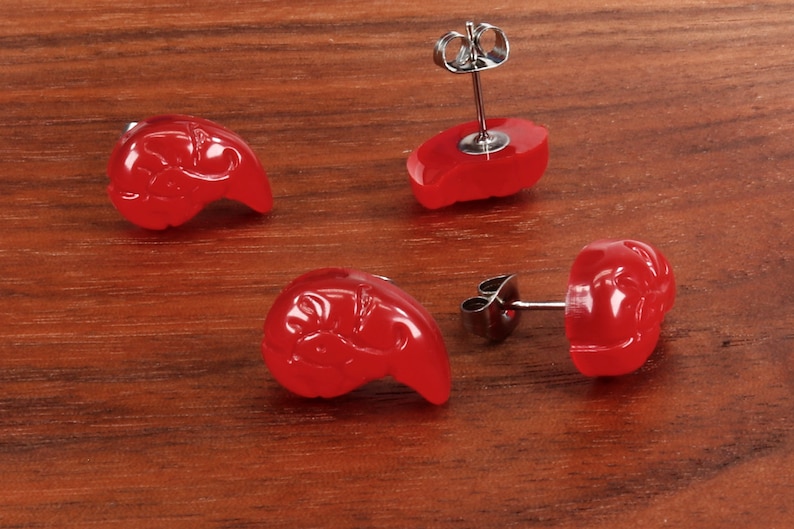 May include: Four red earrings with a floral design. The earrings are made of a smooth, shiny material and have a silver post.