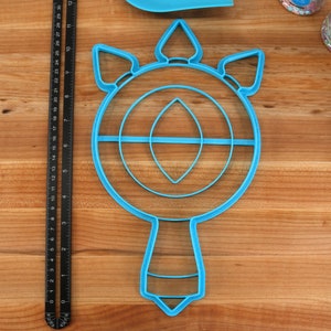 May include: A blue plastic cookie cutter shaped like a unicorn head with a horn and a mane. The cutter has a circular shape with a smaller circle inside and a handle.