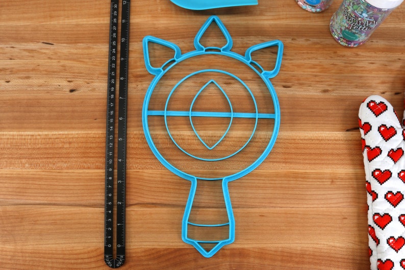 May include: A blue plastic cookie cutter shaped like a unicorn head with a horn and a mane. The cutter has a circular shape with a smaller circle inside and a handle.