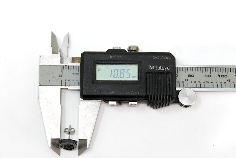 May include: A close-up of a digital caliper measuring a small black earring. The caliper reads 10.85 mm.