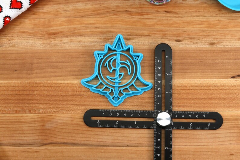 May include: A blue plastic cookie cutter shaped like a stylized symbol with a circular design and a central point. The cutter is approximately 2 inches in diameter.