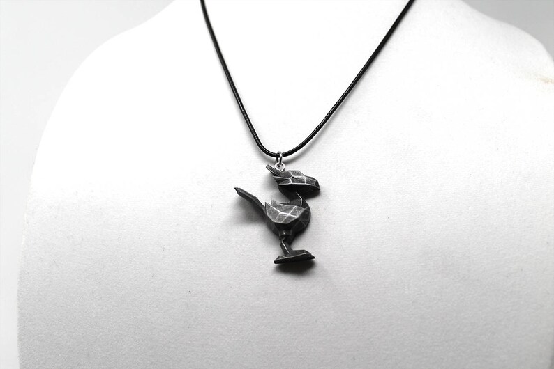May include: A black necklace with a geometric bird pendant. The bird is made of a dark gray material and has a detailed design.