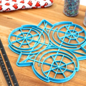 May include: A blue plastic cookie cutter with three circular designs. Each design has a circular pattern of lines radiating from the center.