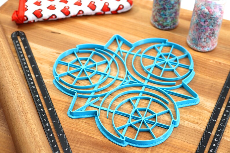 May include: A blue plastic cookie cutter with three circular designs. Each design has a circular pattern of lines radiating from the center.