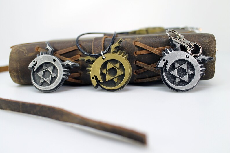 May include: Three metal pendants featuring a stylized dragon design with a star of David inside. The pendants are silver, gold, and bronze in color. The pendants are on a brown leather background.