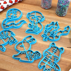 May include: A set of six blue plastic cookie cutters shaped like different animals. The cutters are on a wooden surface.