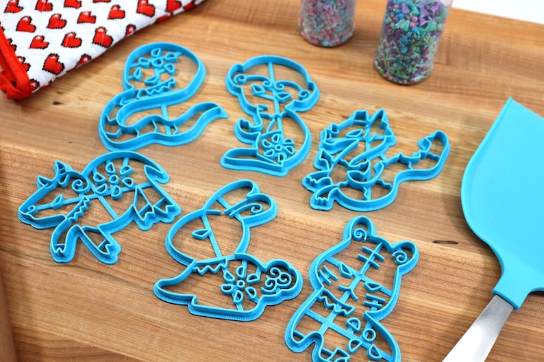 May include: A set of six blue plastic cookie cutters shaped like different animals. The cutters are on a wooden surface.