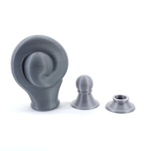 K&ouml;nnte beinhalten: Drei graue 3D-gedruckte Objekte auf wei&szlig;em Hintergrund. Das gr&ouml;&szlig;te Objekt hat ein geschwungenes, spiralf&ouml;rmiges Design. Zwei kleinere Objekte &auml;hneln Schachfiguren, eines mit einem kugelf&ouml;rmigen Kopf und das andere mit einer kreisf&ouml;rmigen &Ouml;ffnung.