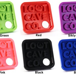 May include: Six square-shaped keychains with the text "LOOT CAVE CO." in raised letters. The keychains are available in six colors: silky green, red, silky purple, pink, black, and blue.