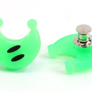 May include: A pair of green plastic crescent moon shaped buttons with black eyes. One button has a metal pin back.