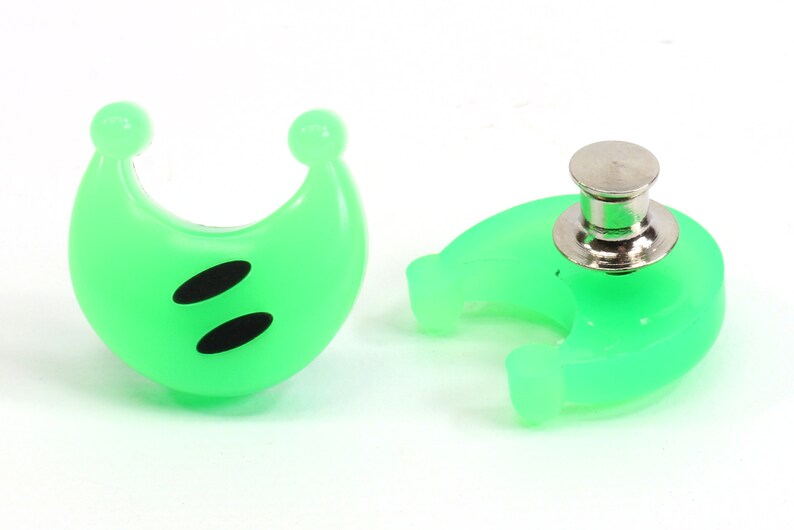 May include: A pair of green plastic crescent moon shaped buttons with black eyes. One button has a metal pin back.