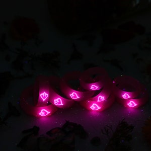 May include: A stack of pink silicone rings with a heart design. The rings are glowing in the dark.
