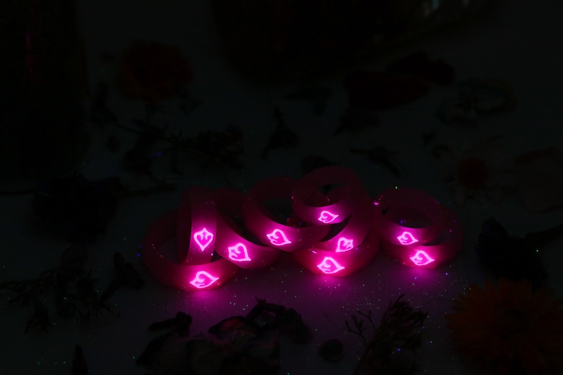 May include: A stack of pink silicone rings with a heart design. The rings are glowing in the dark.