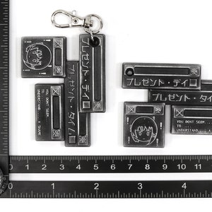 May include: A silver metal keychain with a series of connected rectangular charms. The charms feature Japanese text, a cartoon character, and the phrase "You don't seem... to... understand... A shame."