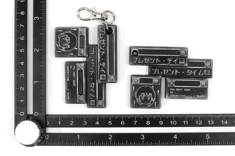 May include: A silver metal keychain with a series of connected rectangular charms. The charms feature Japanese text, a cartoon character, and the phrase "You don't seem... to... understand... A shame."