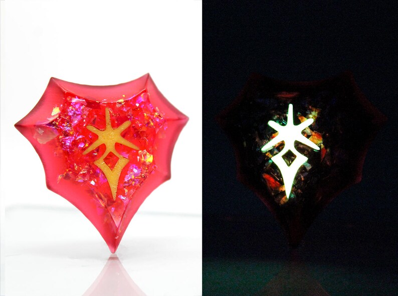May include: A red, heart-shaped resin pendant with a gold-colored symbol inside. The pendant glows in the dark, revealing a white symbol.