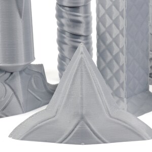 Puede incluir: Primer plano de una forma geom&eacute;trica gris, impresa en 3D, con una parte superior puntiaguda y una base en forma de estrella. La forma est&aacute; hecha de un material liso, similar al pl&aacute;stico.
